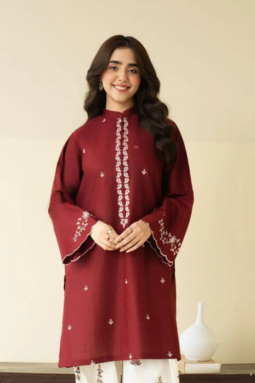 Woman wearing a maroon embroidered top and white pants against a beige background